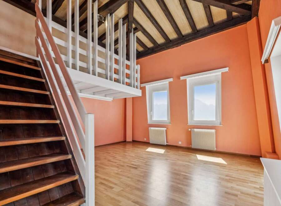 Discover this charming attic space featuring a rustic wooden staircase leading to a loft area with white railings.