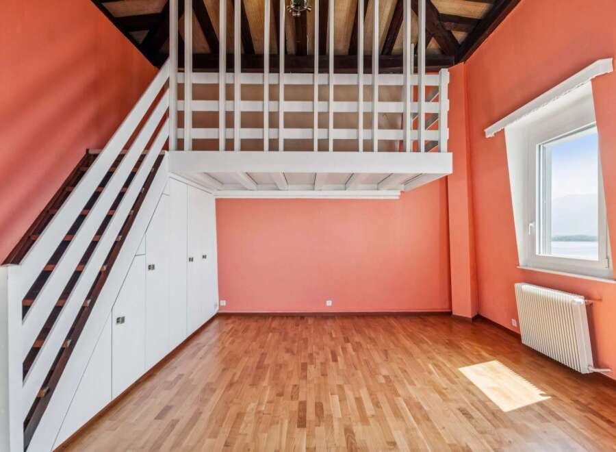 Discover this charming loft space featuring a white railing overlooking the room and a wooden staircase leading to the upper level.
