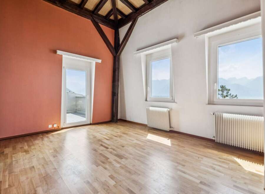 Experience breathtaking mountain views from this spacious room featuring a charming salmon-colored accent wall and a glass door leading to a balcony.