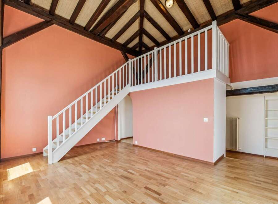 Discover this charming loft-style space featuring a striking salmon-pink accent wall and exposed wooden beams, creating a warm and inviting atmosphere.