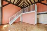 Discover this charming loft-style space featuring a striking salmon-pink accent wall and exposed wooden beams, creating a warm and inviting atmosphere.