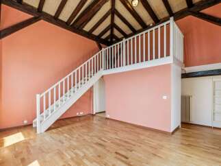 Discover this charming loft-style space featuring a striking salmon-pink accent wall and exposed wooden beams, creating a warm and inviting atmosphere.