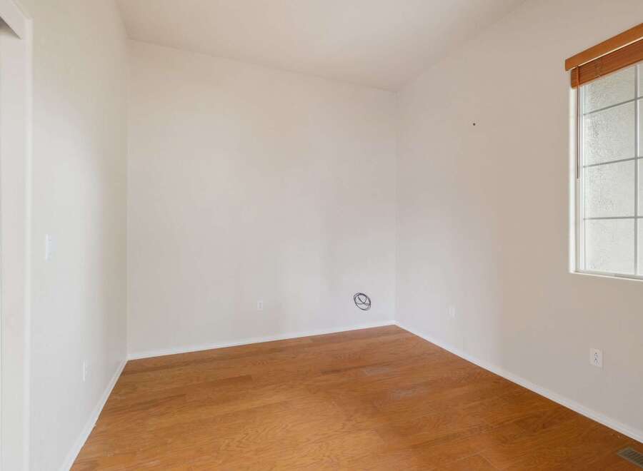 This empty room features a clean, neutral palette with white walls and a warm, polished hardwood floor.