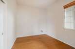 This empty room features a clean, neutral palette with white walls and a warm, polished hardwood floor.