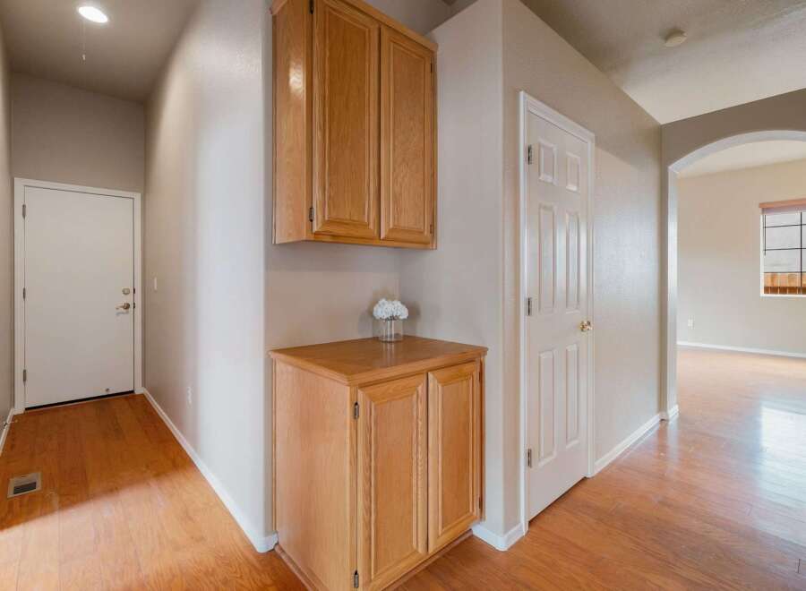This hallway features beautiful hardwood floors that lead to a white door on the left and a set of wooden cabinets on the right.