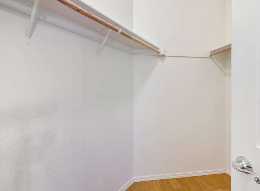 Step into this spacious walk-in closet, featuring a sturdy wooden rod and ample shelving for all your storage needs.