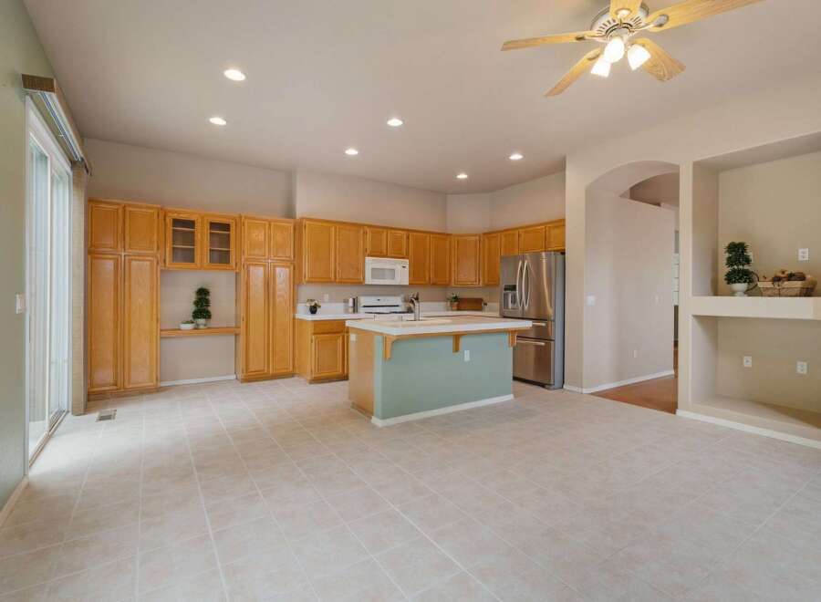 This spacious kitchen features ample natural light, complemented by warm oak cabinetry and a central island with a light green base.
