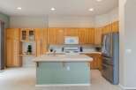 This spacious kitchen features light wood cabinetry, a large island with a tiled countertop, and a stainless steel refrigerator.