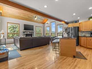Experience breathtaking mountain views from this stunning open-concept living space, featuring a vaulted wood-beamed ceiling and a cozy stone fireplace.