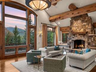 Experience luxury mountain living in this stunning great room, featuring a grand stone fireplace and soaring vaulted ceilings with exposed wooden beams.