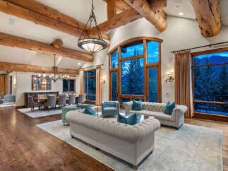 Experience luxurious mountain living in this stunning great room, featuring soaring vaulted ceilings with exposed wooden beams and a grand stone fireplace.