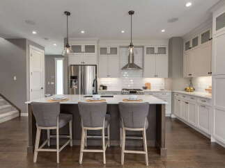 Experience modern luxury in this stunning kitchen, featuring sleek white cabinetry, a spacious island with bar seating, and a professional-grade stainless steel range hood.