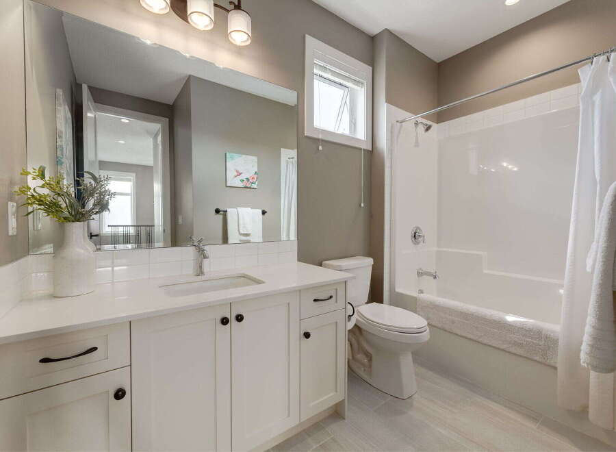 This modern bathroom features a sleek white vanity with ample storage and a large mirror, complemented by a clean white toilet and a bathtub with a shower.