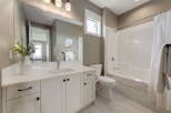 This modern bathroom features a sleek white vanity with ample storage and a large mirror, complemented by a clean white toilet and a bathtub with a shower.