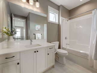 This modern bathroom features a sleek white vanity with ample storage and a large mirror, complemented by a clean white toilet and a bathtub with a shower.
