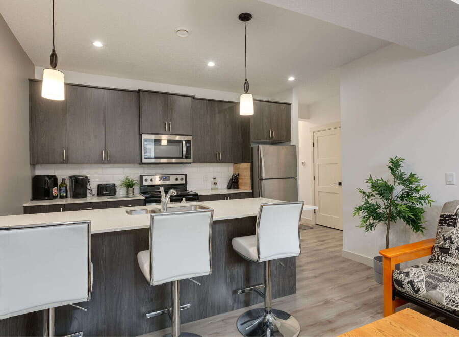 This modern kitchen features sleek dark wood cabinetry, a stainless steel appliance suite including a microwave and refrigerator, and a spacious island with white bar stools perfect for casual dining.