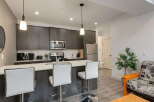 This modern kitchen features sleek dark wood cabinetry, a stainless steel appliance suite including a microwave and refrigerator, and a spacious island with white bar stools perfect for casual dining.