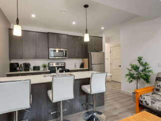 This modern kitchen features sleek dark wood cabinetry, a stainless steel appliance suite including a microwave and refrigerator, and a spacious island with white bar stools perfect for casual dining.