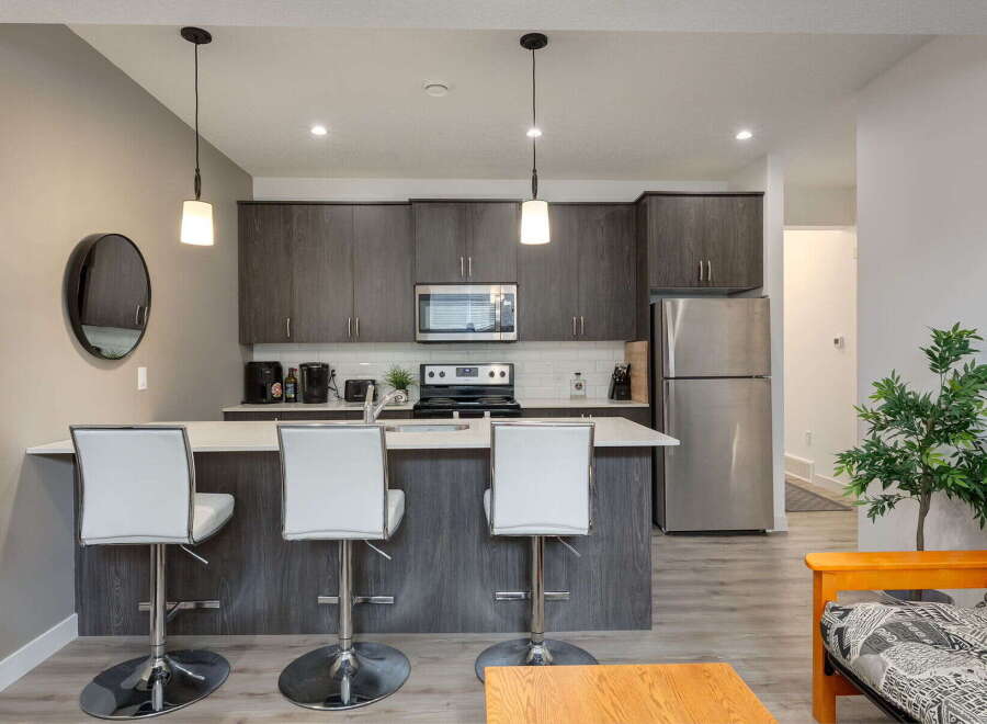 This modern kitchen features sleek, dark wood cabinetry and a spacious island with white bar stools, perfect for casual dining or entertaining.