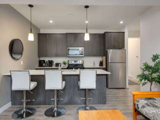 This modern kitchen features sleek, dark wood cabinetry and a spacious island with white bar stools, perfect for casual dining or entertaining.