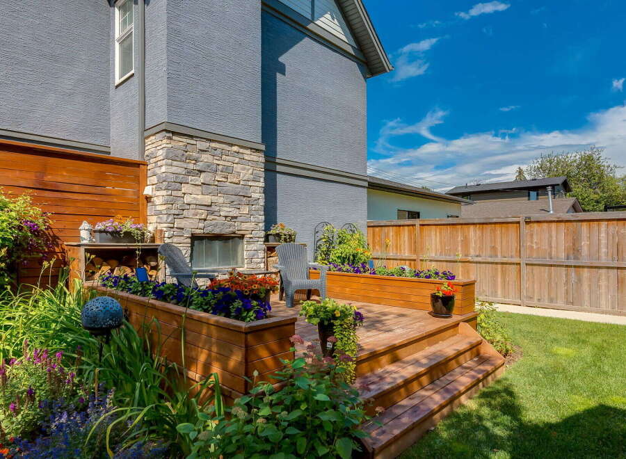 Enjoy outdoor living in this beautifully landscaped backyard featuring a multi-level wooden deck with built-in planters overflowing with colorful flowers.