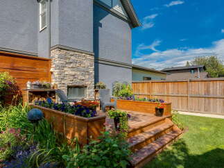 Enjoy outdoor living in this beautifully landscaped backyard featuring a multi-level wooden deck with built-in planters overflowing with colorful flowers.