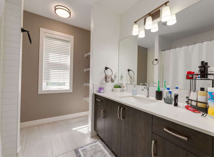 This modern bathroom features a sleek dark wood vanity with a white quartz countertop, offering ample storage and a clean aesthetic.