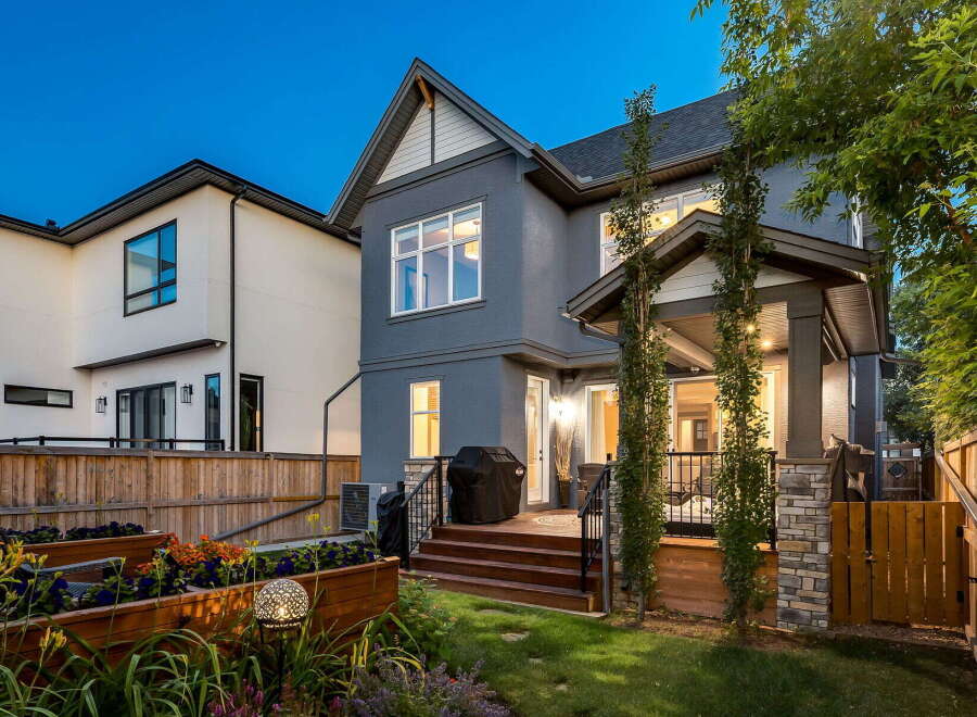 This stunning backyard features a modern grey stucco house with a covered porch and a wooden deck, perfect for outdoor entertaining.