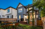 This stunning backyard features a modern grey stucco house with a covered porch and a wooden deck, perfect for outdoor entertaining.