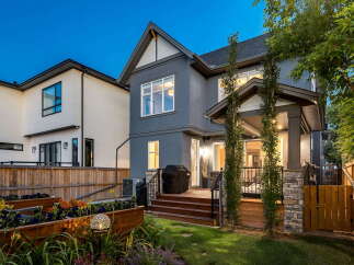 This stunning backyard features a modern grey stucco house with a covered porch and a wooden deck, perfect for outdoor entertaining.