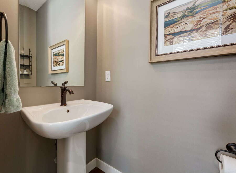 This powder room features a stylish pedestal sink with a bronze faucet, complemented by a large vanity mirror.