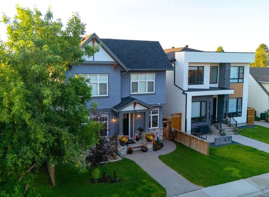 Discover modern living in this stunning blue stucco home, featuring a welcoming covered porch with stone accents and ample natural light through large windows.