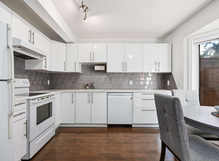 This modern kitchen features sleek white cabinetry and a stylish gray subway tile backsplash.