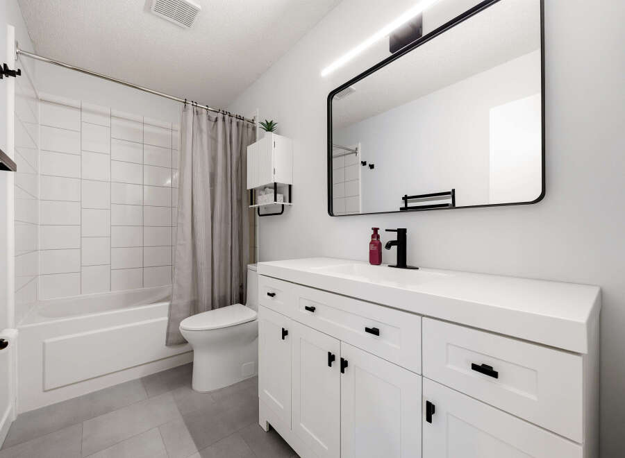 This modern bathroom features a sleek white vanity with black hardware, complemented by a large black-framed mirror and a stylish black faucet.