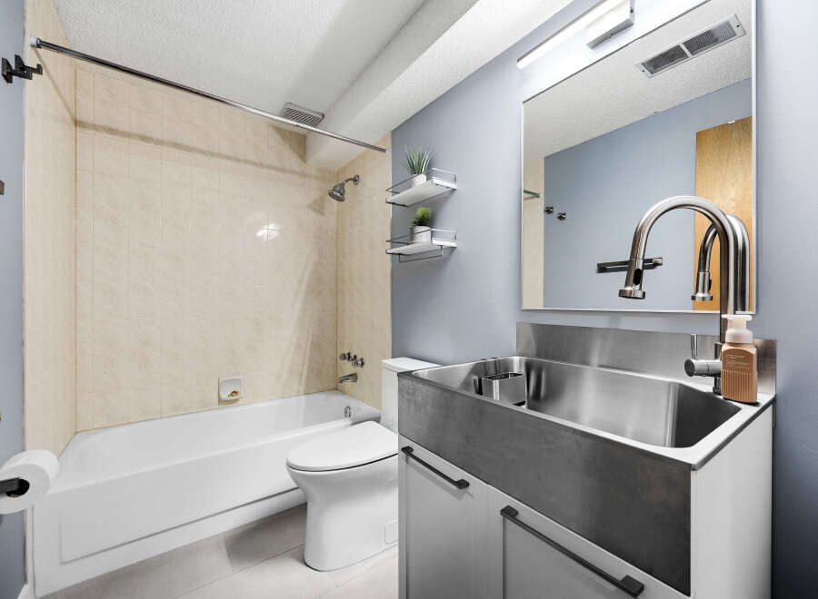 This modern bathroom features a sleek stainless steel sink and vanity, complemented by a large mirror and a stylish faucet.