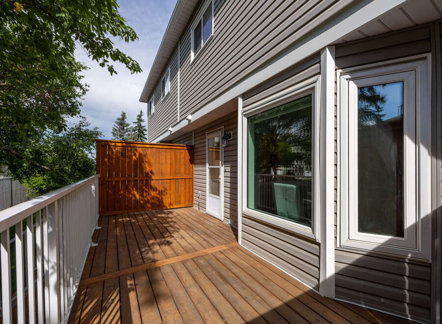 Enjoy outdoor living on this spacious wooden deck, complete with a white railing and a privacy screen.