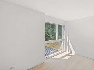 Bathed in natural light, this empty room features a large window offering serene views of lush greenery.
