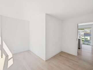 Step into this bright and airy room, featuring pristine white walls and elegant light wood flooring that enhances the natural light streaming in from the large window.