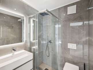 Experience modern luxury in this stunning bathroom featuring sleek grey marble tiles and a spacious glass-enclosed shower.