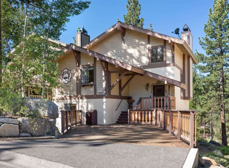 Nestled amidst tall pine trees, this charming mountain home offers a unique alpine-inspired exterior with a decorative crest and warm wood accents.