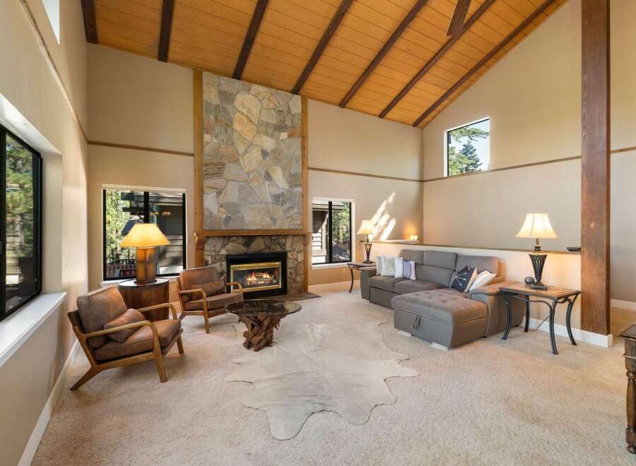 Experience rustic charm in this spacious living room featuring a grand stone fireplace and soaring vaulted ceilings with exposed wooden beams.