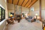 Experience rustic charm in this spacious living room featuring a grand stone fireplace and soaring vaulted ceilings with exposed wooden beams.