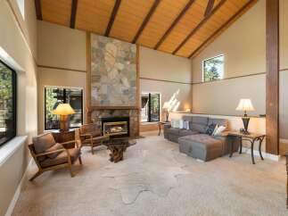 Experience rustic charm in this spacious living room featuring a grand stone fireplace and soaring vaulted ceilings with exposed wooden beams.