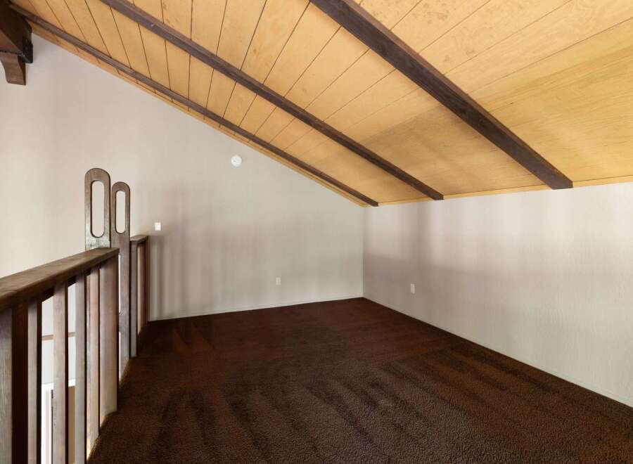 Discover this charming loft space featuring a vaulted wood-paneled ceiling with exposed beams, creating a warm and inviting atmosphere.