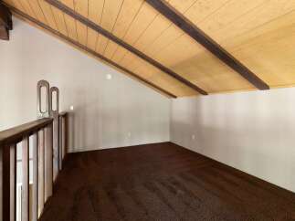 Discover this charming loft space featuring a vaulted wood-paneled ceiling with exposed beams, creating a warm and inviting atmosphere.