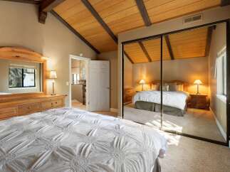 Experience ultimate comfort in this spacious bedroom, featuring a vaulted wood-beam ceiling and a large mirrored closet.