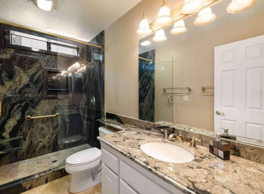 Experience luxury in this stunning bathroom featuring a spacious walk-in shower with intricate granite tile and a convenient built-in bench.
