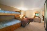 This spacious bedroom comfortably sleeps up to six guests, featuring a sturdy wooden bunk bed and two additional twin beds.