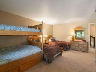 This spacious bedroom comfortably sleeps up to six guests, featuring a sturdy wooden bunk bed and two additional twin beds.