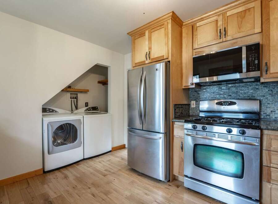 This kitchen features a stainless steel refrigerator, a gas range with a microwave above, and a stacked washer and dryer tucked into a convenient alcove.